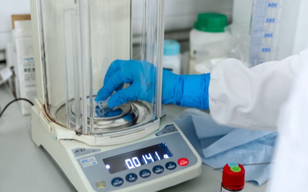 Gloved hand weighing powder on an analytical balance in a laboratory