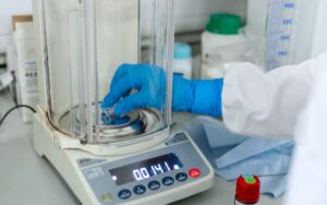 Gloved hand weighing powder on an analytical balance in a laboratory