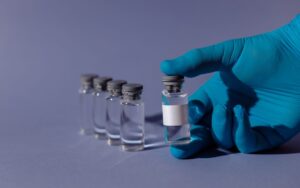 Gloved hand holding a clear glass vial beside a row of laboratory vials